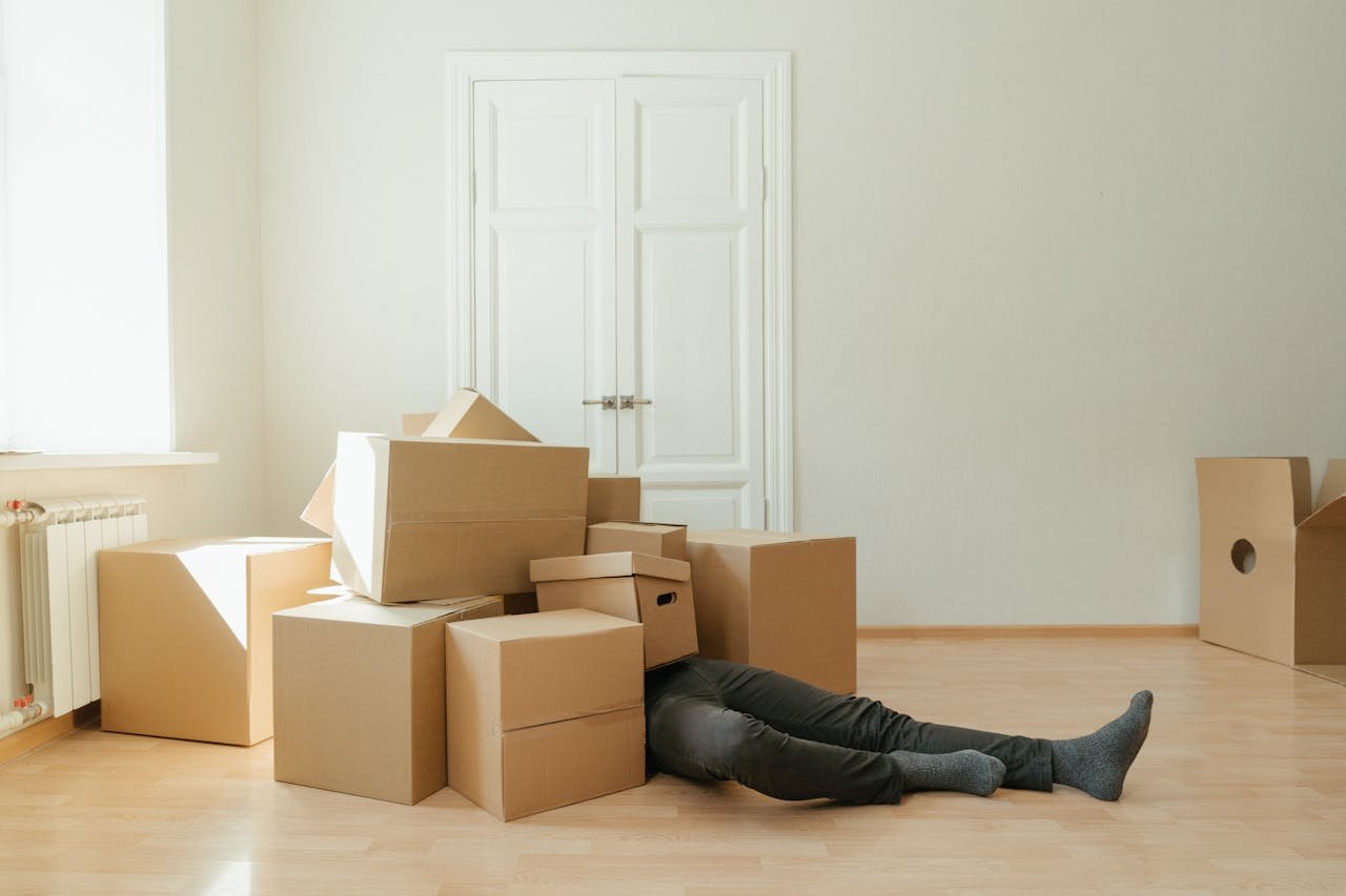 hero-img Person on floor surrounded by cardboard boxes during moving; concept of stress and relocation.