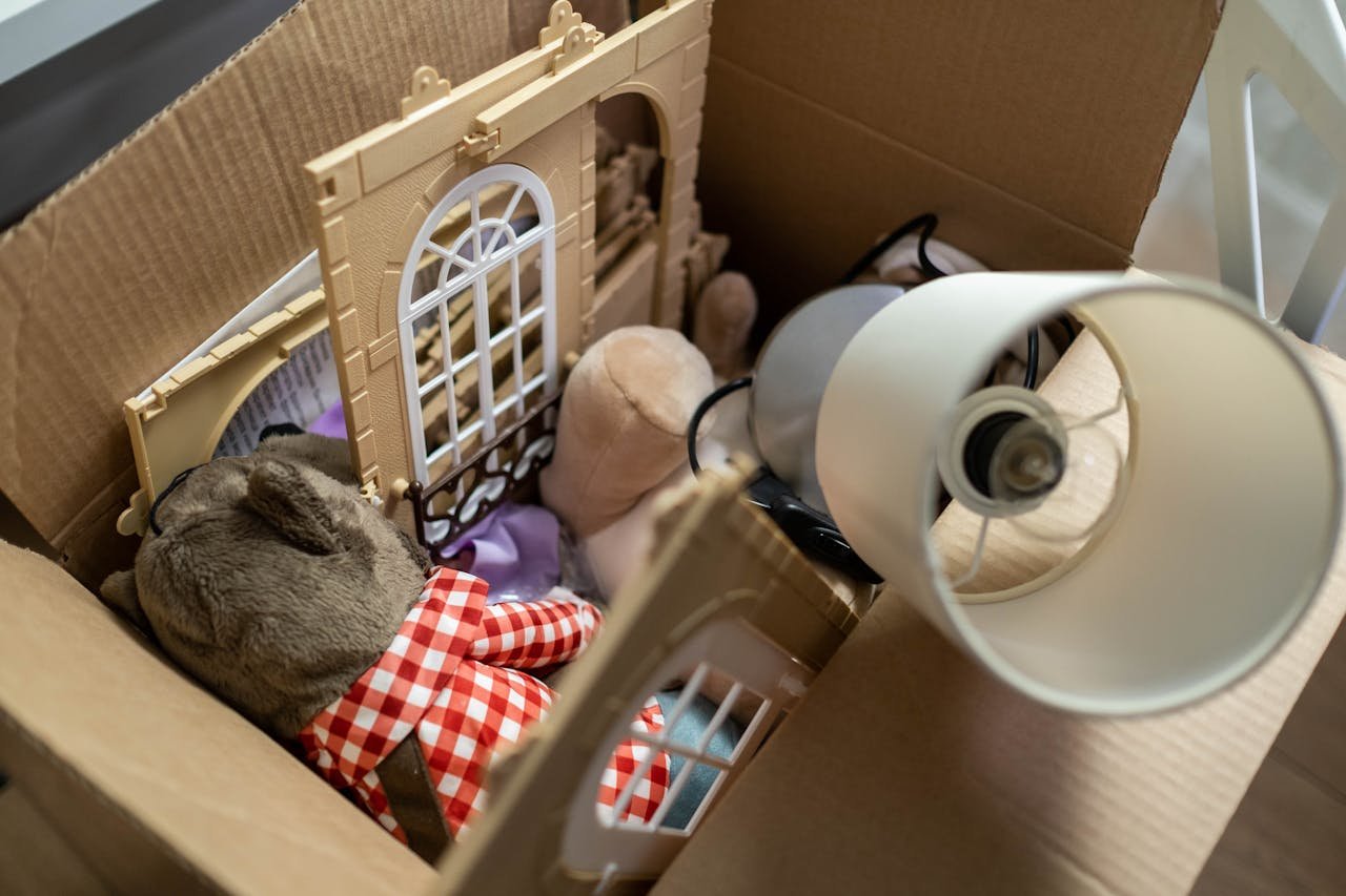 Cardboard box containing toys and a lampshade, perfect for moving or storage themes.