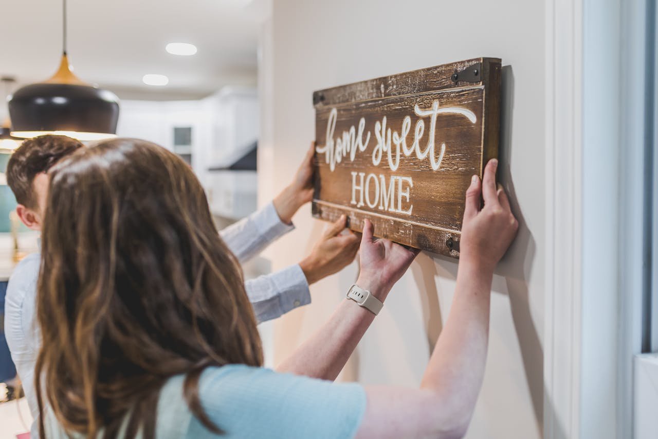 Couple hanging a 'Home Sweet Home' sign indoors, embodying a cozy and welcoming atmosphere.